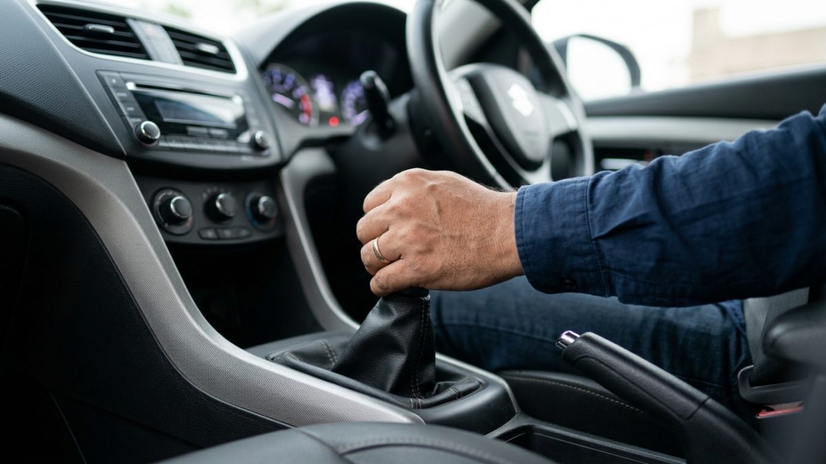 Driver manually shifting gears smoothly inside a car to optimize fuel efficiency